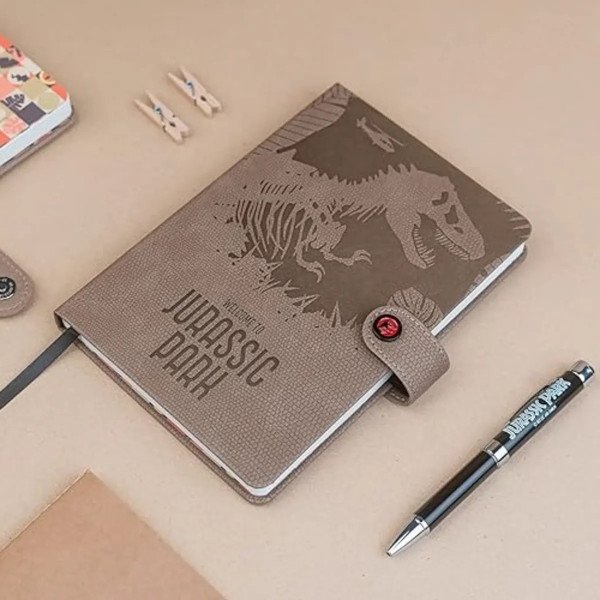 Carnet premium A5 Jurassic Park avec stylo projecteur posé à côté sur bureau beige.