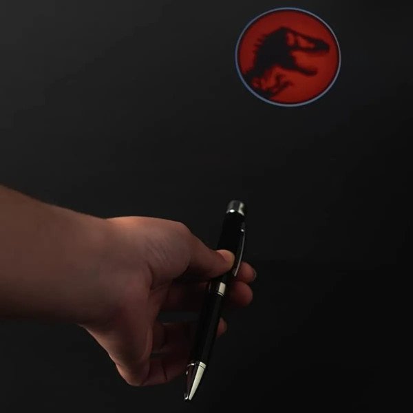 Stylo projecteur Jurassic Park projetant le logo rouge du T-Rex sur fond noir.