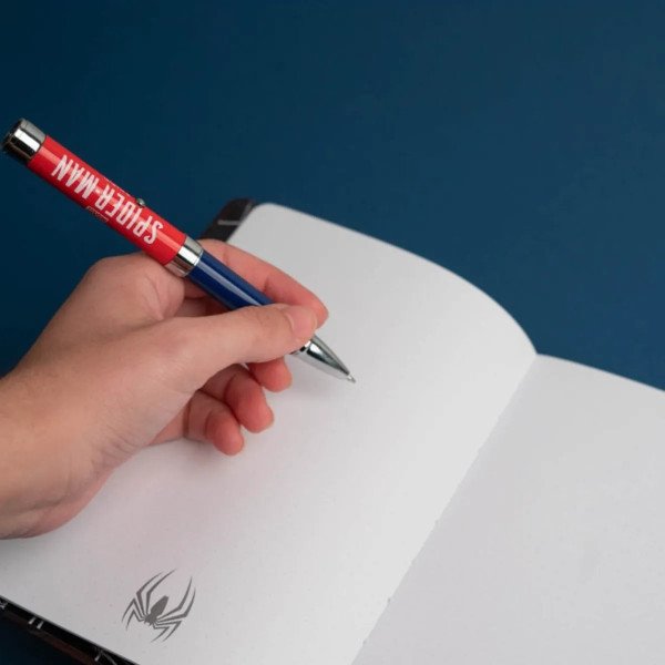 Main tenant le stylo projecteur Marvel Spider-Man au-dessus du carnet premium A5 ouvert.