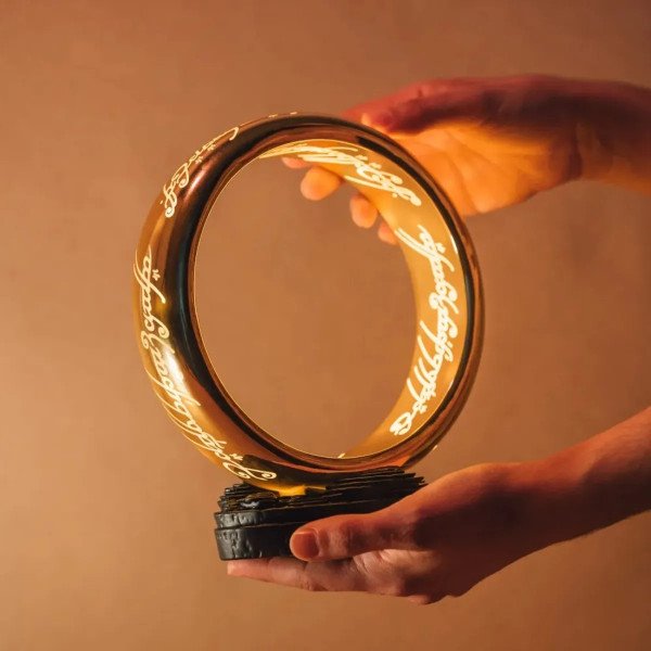 Lampe One Ring Le Seigneur des Anneaux allumée, tenue à la main avec lumière dorée chaude.