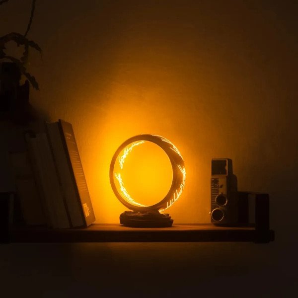 Lampe One Ring allumée sur une étagère sombre, avec halo doré façon objet de collection.