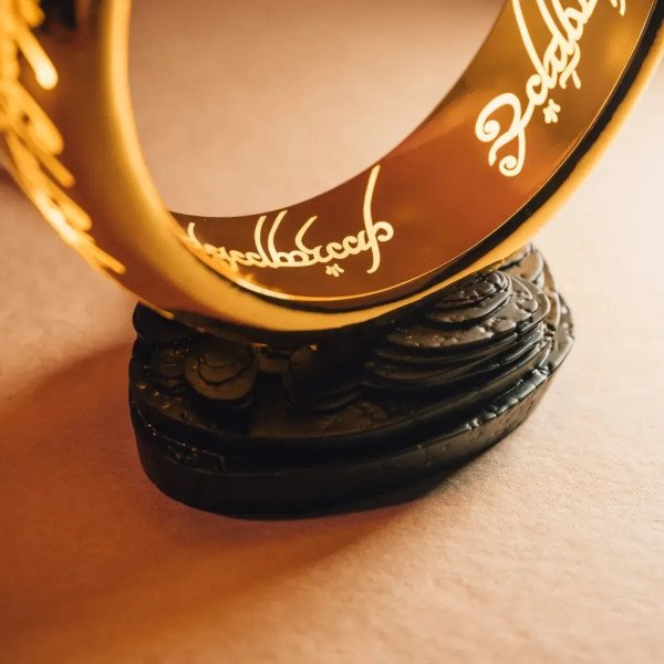 Gros plan sur la lampe One Ring dorée avec inscription elfique lumineuse et socle noir.