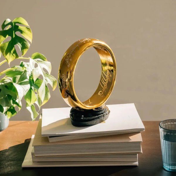 Lampe One Ring Le Seigneur des Anneaux posée sur des livres, avec plante et lumière naturelle.